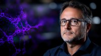 Middle-aged man with dark hair and glasses wearing black shirt against blurred background with purple glowing molecular structure, representing science, technology, research, and innovation concepts.