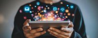 Hands holding smartphone with glowing social media and application icons floating above screen, depicting digital connectivity and mobile technology in dark setting.