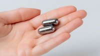 Silver metallic capsules or pills held in open palm against light background, demonstrating medical supplement or pharmaceutical product for healthcare marketing.
