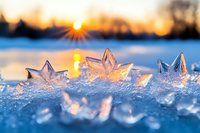 Delicate ice crystals in star shapes glisten on frozen surface at sunset, creating magical winter scene with golden sunburst and bokeh reflections on crystalline snow.