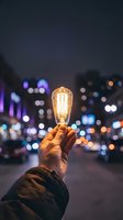 Hand holding glowing vintage Edison bulb against blurred city lights at night showcasing innovation and creativity concepts for business presentations.