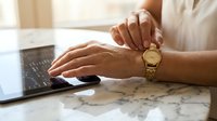 Professional woman hands typing on laptop computer wearing elegant gold watch at marble desk workspace for business productivity and time management.