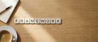 Wooden letter blocks spelling FRAMEWORK on desk with coffee cup and notebooks for business planning and organizational strategy concepts.