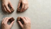Hands arranging wooden dice with cryptocurrency symbols on neutral linen background for financial planning and digital investment concepts.