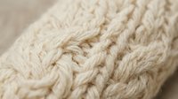 Close-up of cream cable knit wool texture showing intricate braided pattern and soft fibers for cozy winter fashion and textile design projects.