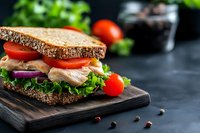 Fresh turkey sandwich with lettuce tomato and red onion on multigrain bread served on wooden cutting board for healthy lunch meal preparation.