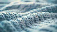 Close up macro view of soft knitted fabric texture in light blue color showing detailed wool or cotton yarn pattern with selective focus effect.