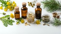 Amber glass bottles, herbal capsules, and dried plants arranged on white background for natural medicine and wellness concepts.