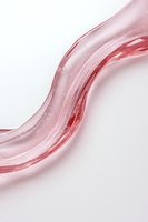 Elegant flowing pink liquid wave with glossy translucent texture creates dynamic curved shape against white background, suitable for cosmetic and beauty designs.