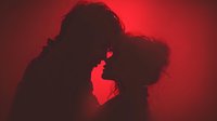 Romantic couple silhouette kissing in passionate embrace against dramatic red lighting for Valentine's Day and love themed designs.