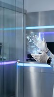 Scientist in white gloves and lab coat interacting with holographic display showing digital data visualization in modern laboratory setting with neon blue lighting.