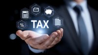 Businessman holding glowing tax concept with financial icons floating above hand against dark background, representing digital taxation and financial management.