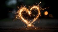Glowing sparkler heart shape with golden sparks against dark blurred background. Romantic celebration concept for Valentine's Day, weddings, anniversaries.