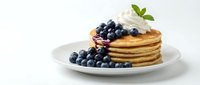 Stack of golden pancakes topped with fresh blueberries, whipped cream, and mint leaves on white plate for breakfast, brunch, or dessert recipes.