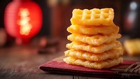 Stack of crispy square butter waffles on dark rustic wooden table with red bokeh light in background, selective focus on golden pastry texture.