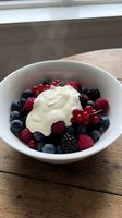 Fresh mixed berries with cream in white bowl on rustic wooden table for healthy breakfast dessert concept.