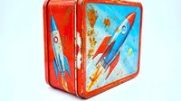Vintage red metal lunch box with retro rocket ship space theme design for nostalgic childhood memories and collectible items.