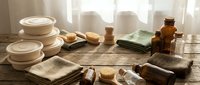 Eco-friendly zero waste bathroom essentials with bamboo toothbrushes, glass jars, natural soap bars and organic cotton towels on wooden surface.
