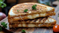 Grilled cheese sandwich with melted mozzarella and caramelized onions, stacked and cut diagonally on wooden board, garnished with fresh parsley and cherry tomatoes.