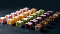 Colorful assorted Turkish delight lokum candy cubes arranged in rows on dark slate background. Traditional Middle Eastern sweets with various flavors and textures.