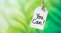 White paper tag with motivational You Can message hanging on string against soft green blurred natural background for inspiration and encouragement concepts.
