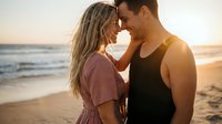 Young couple sharing intimate moment on beach at golden hour sunset with ocean waves in background for romantic lifestyle photography.