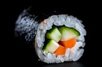 Fresh sushi roll with cucumber, carrot and avocado wrapped in nori seaweed and white rice, close-up macro shot on black background.