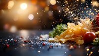 Crispy potato chips with sea salt sprinkled in motion, fresh cherry tomatoes and herbs on dark background with golden bokeh lights and copy space.
