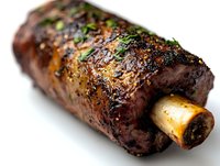 Grilled beef short rib with marrow bone, glazed in savory Asian-inspired sauce and garnished with fresh herbs, photographed on white background with selective focus.