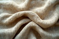 Natural linen fabric with visible texture and waves creates soft folds and shadows on beige burlap material, showing detailed weave pattern and organic curves.