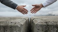 Two businesspeople reaching across concrete gap for handshake symbolizing partnership, cooperation, teamwork and bridging differences in professional setting.