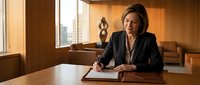 Professional businesswoman writing documents in modern office conference room with city view and warm lighting for corporate presentations.