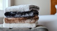 Stack of soft plush faux fur blankets in neutral colors white, brown and gray folded neatly on cozy sofa, creating cozy home atmosphere for interior design.