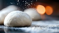 Raw dough ball on floured surface with bokeh lights in background, macro food photography showing texture and flour dust in dramatic lighting.