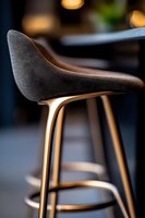 Modern bar stool with curved black leather seat and elegant gold metal base captured in soft ambient lighting, showcasing luxury interior design detail.