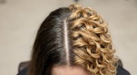 Professional blonde curly hairstyle with dark roots showing natural hair growth and styling technique for beauty salon and hair care concepts.