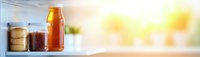 Glass jars with preserved food and honey on kitchen shelf with warm sunlight streaming through window creating cozy domestic atmosphere for cooking.