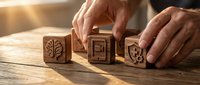 Hands arranging wooden blocks with brain, lightbulb and gear icons on rustic table in warm sunlight representing innovation and creative thinking process.
