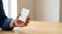 Person holding blank white business card in hand at wooden table, suitable for corporate branding and professional networking presentations.