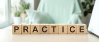 Wooden letter blocks spelling PRACTICE on desk in bright office workspace with laptop and plants creating motivational business concept.