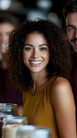 Young African American woman with curly hair wearing yellow sleeveless top smiling brightly at casual restaurant gathering with friends, natural lifestyle portrait.