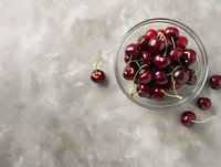 Fresh ripe dark red cherries with stems in glass bowl on gray concrete background with copy space, top view. Food photography styling.