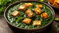 Palak paneer curry with crispy golden cheese cubes in dark ceramic bowl, garnished with fresh herbs on rustic background, traditional Indian cuisine.