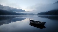 Serene mountain lake with wooden boat floating on calm reflective water surrounded by misty peaks at dawn creating peaceful atmospheric landscape.