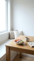 Minimalist breakfast setup with wooden table, bowl of fresh fruit and yogurt, ceramic mug, and window seat with cushions in bright natural light for lifestyle and wellness content.