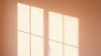 Warm sunlight streaming through window panes casting geometric shadows on peachy beige wall, creating soft natural light effect for interior design and architectural backgrounds.
