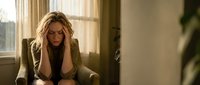 Stressed blonde businesswoman holding head in hands sitting on couch in modern office interior during difficult workday experiencing burnout.
