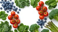 Fresh organic vegetables and blueberries arranged in circle frame on white background. Healthy eating concept with tomatoes, broccoli, spinach, kale, asparagus.