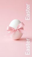 White Easter egg with a delicate pink satin bow on a soft pink background, minimal holiday greeting card concept.