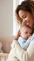 Young African American mother tenderly holding newborn baby in bright nursery room, expressing love and maternal bond in cozy home setting.